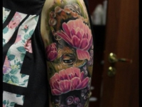 Татуировка взгляд из-за цветов на плече