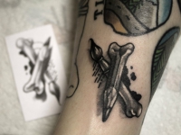 Татуировка карандаш и кисть в виде сложенных костей на руке