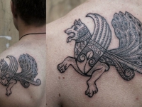 Татуировка собаки с крыльями и хвостом павлина на лопатке